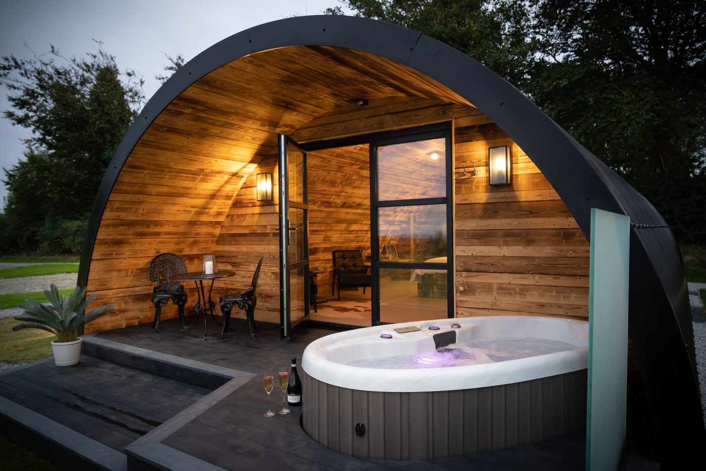 The Piglet Pod hot tub at dusk with champagne glasses and countryside