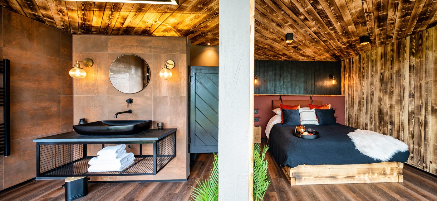 Bathroom and bedroom split — bronze tiles, black vessel sink and velvet-headed bed