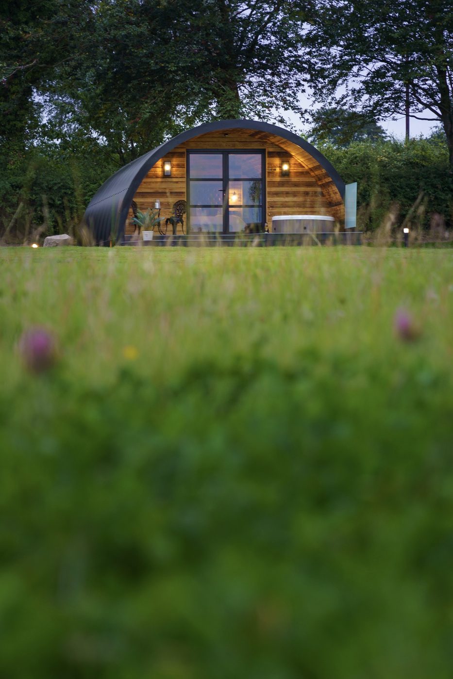 The Piglet Pod seen from the meadow at dusk — warm interior glow