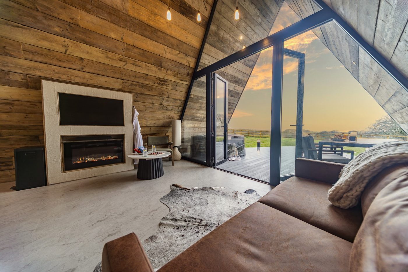 Tri-Pod living room at sunset — bi-fold doors open to countryside, electric fire lit