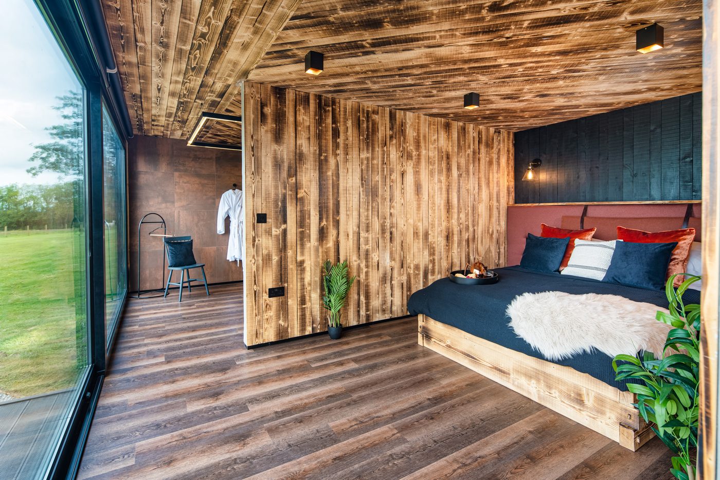 The Rusty Boathouse bedroom — velvet headboard, timber walls, lake view through full-height glass