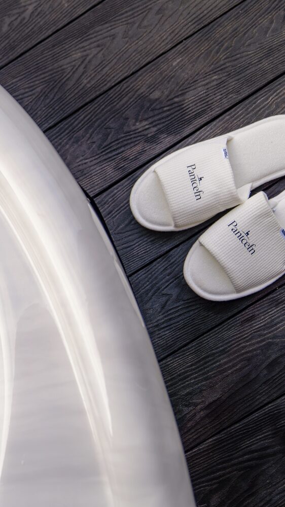 Pantcefn branded slippers beside hot tub on dark timber deck