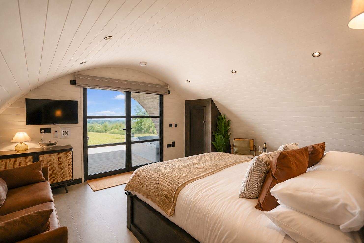 The Hog Hut bedroom with glass doors open to the private deck, hot tub and farmland beyond